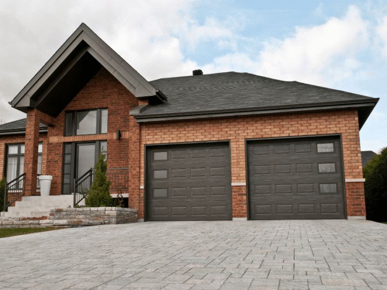 Front view of a brick home with two dark single garage doors featuring raised panels and small windows.